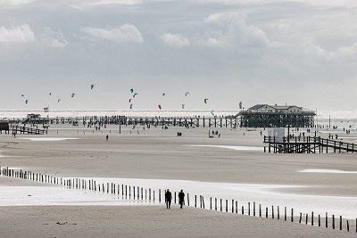 Pfahlbauten und Spaziergaenger am Sandstrand von St. Peter Ording