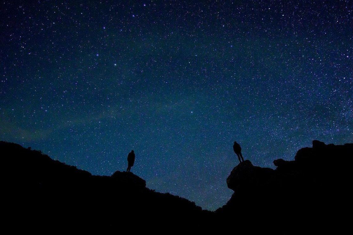 Silhouetten von 2 Personen auf Felsen unter dem Sternenhimmel