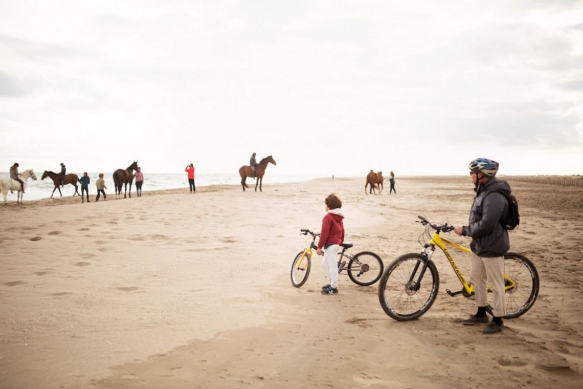 Fahrradfahrer und Reiter am Sandstrand in der Camargue