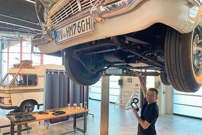 Mitarbeiter Museumswerkstatt unter Oldtimer auf Hebebuehne