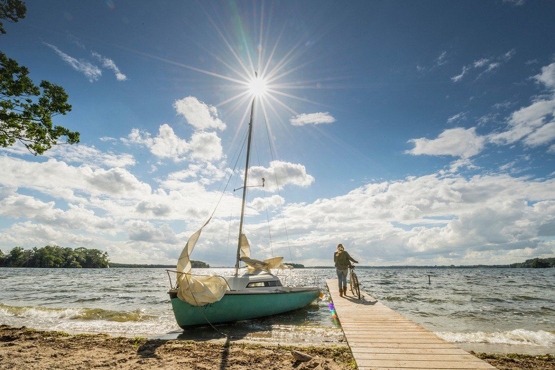 Segelboot und Radfahrer am Strand an der Ostseekueste Schleswig-Holstein
