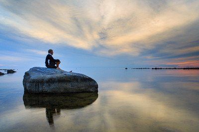 Mann bei Sonnenuntergang im Kvarken Archipel auf Fels sitzend