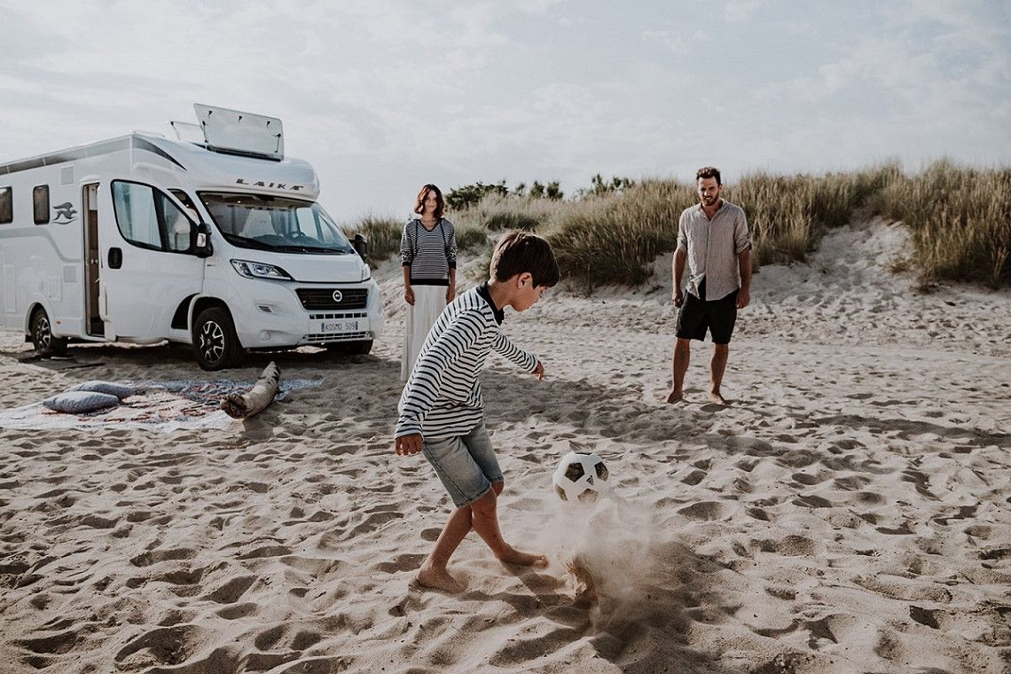 Familie op het strand met camper en voetbal
