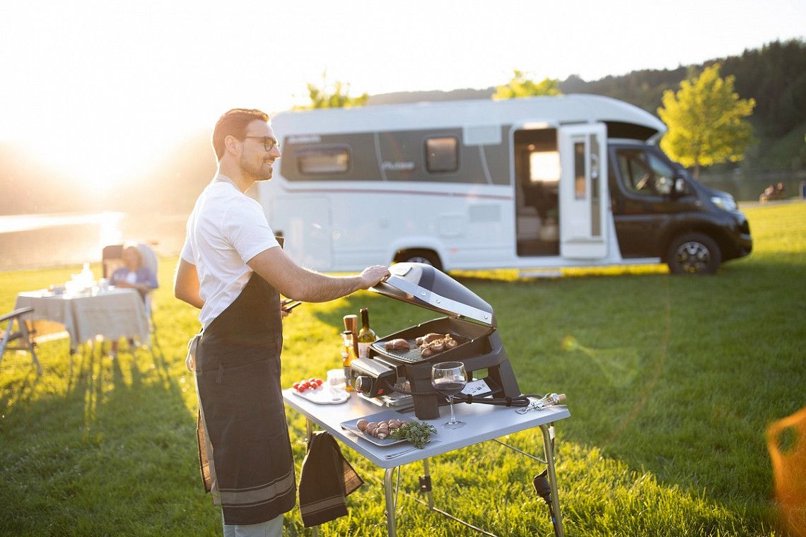 A couple having a barbecue in front of a Dethleffs motorhome