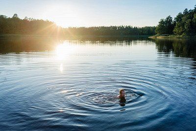Mann schwimmt in schwedischem See bei Mitternachtssonne
