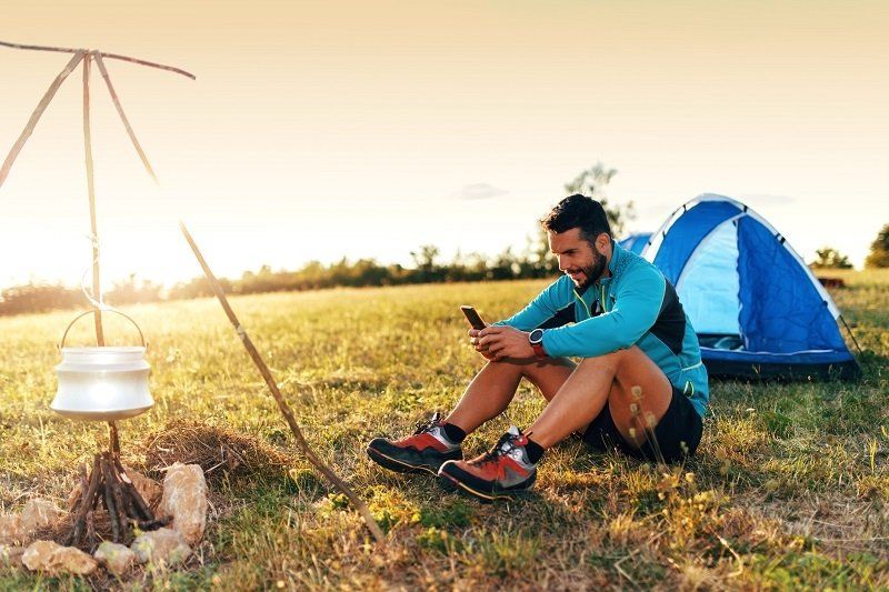 Zelt Camper mit Smartphone auf grüner Wiese 