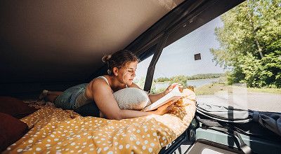 Lesende Frau im Aufstelldach des Bürstner Campervans Campeo Skyline